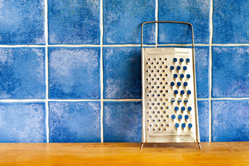 Metal chrome grater for cheese and vegetables on wooden table and blue ceramic tiles