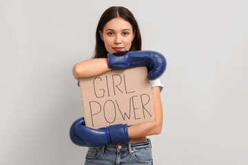 Young woman with sign GIRL POWER and boxing gloves on white background. Feminism concept
