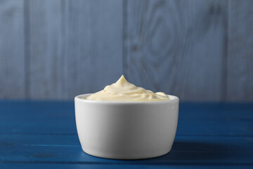 Tasty mayonnaise in bowl on blue wooden table, closeup. Space for text