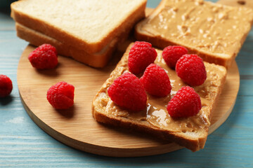Delicious toasts with peanut butter and raspberries on light blue wooden table, closeup