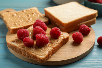 Delicious toasts with peanut butter and raspberries on light blue wooden table, closeup