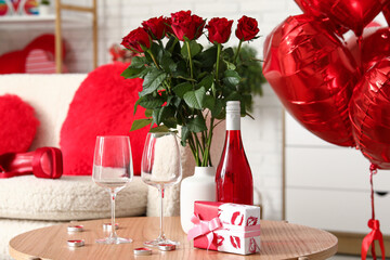 Coffee table with wine bottle, glasses, gift box and bouquet of roses in living room. Valentine's...