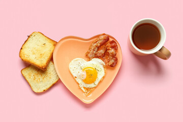 Plate with fried egg, tasty bacon, toasts and cup of tea on pink background