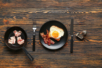 Composition with tasty bacon, heart made of fried egg, toast and cutlery on wooden background