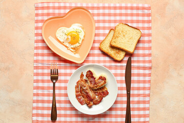 Plates with tasty bacon, heart made of fried egg, toasts and cutlery on beige background