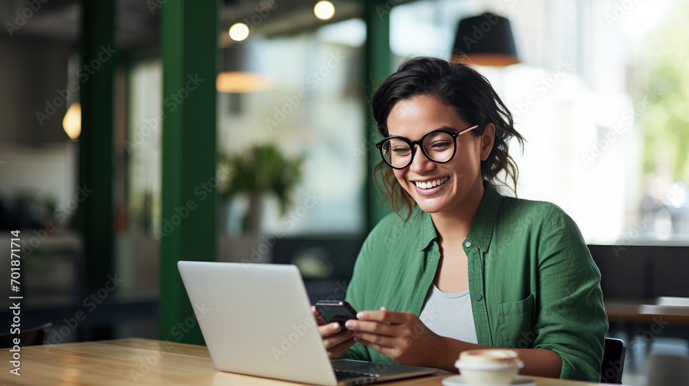 Poster cheerful professional woman wearing glasses and a green blouse is sitting at a desk with a laptop an