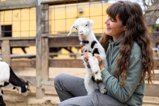 Happy young farmer woman hugging a baby goat on a rural organic farm. Animal welfare and care in a barn.