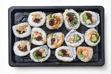 Takeaway sushi background. Uramaki California roll and futomaki. Japanese food isolated on white table. Black sushi takeaway box isolated. Cutout sushi. Different various types of sushi. Lunch box.
