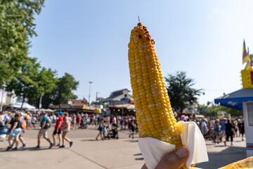 Hand holds up a corn on the cob, to eat at a fair