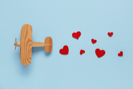 Wooden airplane with paper hearts on blue background. Valentine's Day celebration