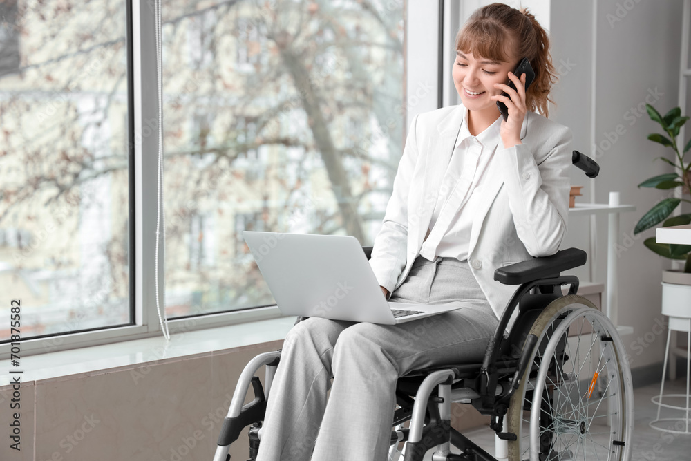 Sticker Young businesswoman in wheelchair with laptop talking by mobile phone at office