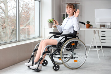 Young businesswoman in wheelchair with mobile phone waving hand at office