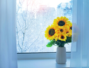 Sunflowers in the winter season on window. Snow-covered trees outside the window. Bright sunflowers against the backdrop of a winter landscape.