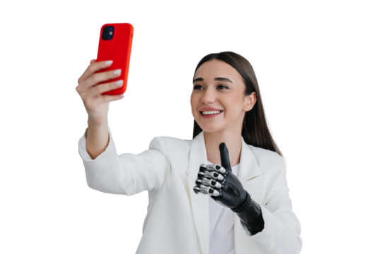 European brunette handicapped girl in white suit holding phone, making video call  showing thumb up gesture by biomechanical prosthesis at office. Cute disabled female toothy smiling, making selfie.