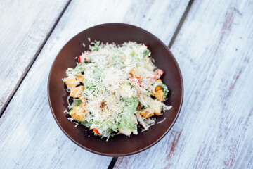 Top view Classical Caesar salad with roasted chiken, quail eggs, lettuce leaves, becon, parmesan slices and cherry tomatoes on the white plate on the white table