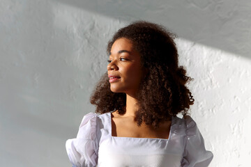 Young tender african american woman with curly hairstyle standing in warm sunlight indoors - obrazy, fototapety, plakaty