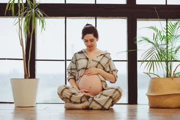 Tuinposter Meditation during pregnancy. Young calm tranquil pregnant woman in lotus pose touching belly © Dasha Petrenko