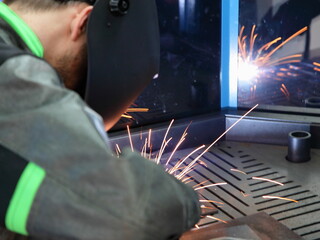 Electric MIG MAG metal welding on welding table. Welder in overalls and a welding mask closeup. Gas...