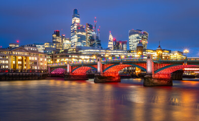 Fototapeta na wymiar Southwark Bridge in english metropole London spanning over river Thames at evening blue hour twilight with colorful illumination at christmas time. Modern skyline with office towers in the background.