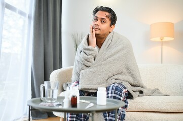 Sick Indian man in plaid sit alone shivering from cold. Unhealthy Arabian guy sit on chair feeling...