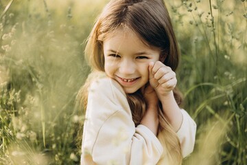 portrait of a cute smiling girl with beautiful hair posing for a photo in the middle of tall grass in a coniferous forest at sunset