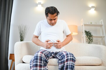 Sad exhausted guy of indian and arabian ethnicity, holds his hands on his stomach, grimaces from pain in his stomach, suffers from poisoning, spasm, stomach problems