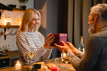 Happy mature couple sharing presents for anniversary or St. Valentines day during romantic dinner...