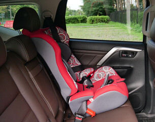 Red infant car seat in the back seat secured with standard seat belts
