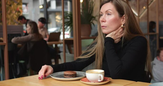 Sad lonely beautiful mid age woman sits with distant look alone in urban cafe. Young woman with long brown hair sitting in solitude at table with coffee and dessert in coffee shop. 4k footage.
