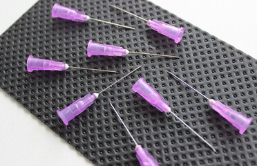 Open needles for disposable syringes are scattered on a black medical napkin