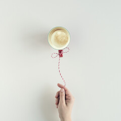 Woman hand with Inflatable air flying balloon made from cup of coffee hanging on a red white string or twine tied in a bow. White table. Christmas Concept. Creative