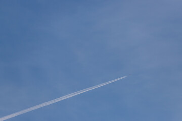 A large airliner flies in the air. There are white clouds and a trail behind the plane in the blue...
