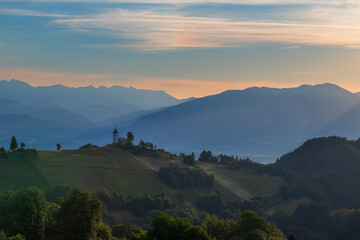 Church of Saint Primoz in Jamnik village, Slovenia, Europe. The church is on the ridge of the mountains. Sunrise, mountain peaks in the background.