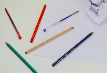 A photo of a student's coloring pencils and pieces of white paper scrunched up on a white desk.