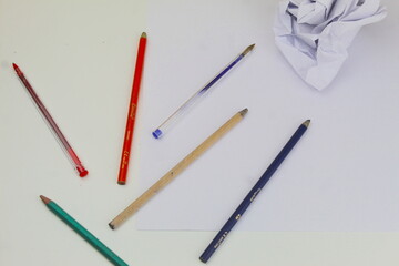 A photo of a student's coloring pencils and pieces of white paper scrunched up on a white desk.