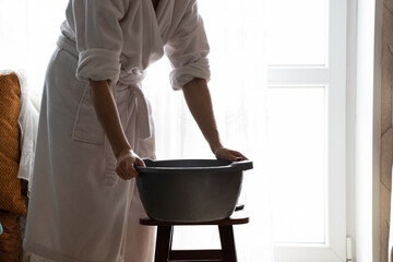 A girl in a bathrobe puts a plastic bowl on a chair to wash her hair, lifestyle
