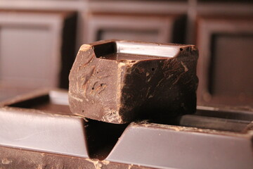 A bar of dark bitter chocolate with a piece of chocolate in the foreground, that is used to make...