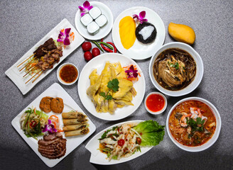Assorted thai food with grilled pork neck, fish cake, spring roll, chicken feet, beef and chicken satay, sago cake, sticky rice with mango served isolated on background top view of hong kong food