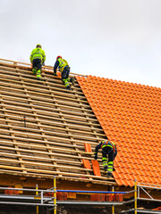 Three workers in protective workwear installing new clay tiles roof, new clay tiles layer covering