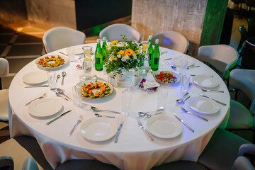 beautifully arranged round banquet table set for a formal dining event. The table is dressed with a crisp white tablecloth and is set with white plates, silverware, and clear glasses