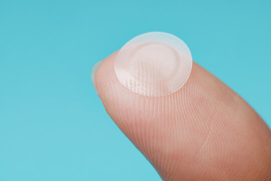 Close-up round acne patch on finger on blue background. Acne patches for treatment of pimple and rosacea close-up. Facial rejuvenation cleansing cosmetology