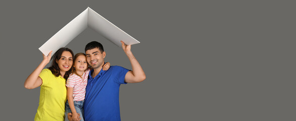 Happy family with cardboard in shape of roof dreaming about their new house on grey background with...