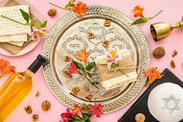 Composition with Passover Seder plate, flatbread matza, bottle of wine, Torah and flowers on pink background
