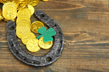 Horseshoe with golden coins and paper clover on brown wooden background. St. Patrick's Day celebration