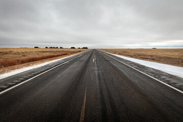 Northern Plaines Nebraska flat lonesome highway in winter with clouds on the horizon.