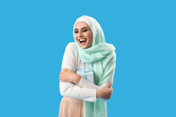 Young Muslim woman with gift on blue background. Islamic New Year celebration