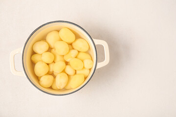 Pot with peeled potatoes on light background