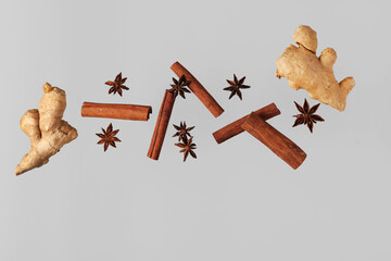 Flying cinnamon sticks, anise stars and ginger roots on grey background - obrazy, fototapety, plakaty