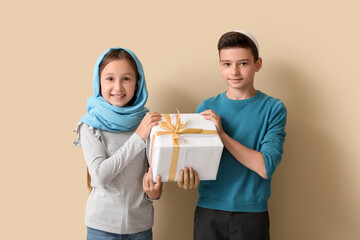 Little Muslim children with gift on beige background