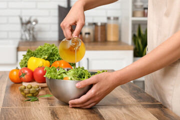 Woman adding olive oil into bowl with tasty salad at table in kitchen